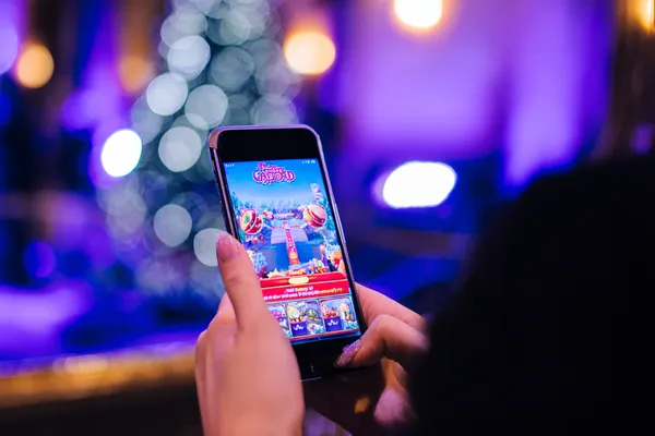 Uma jovem relaxando com o celular enquanto elementos dinâmicos de cassino flutuam ao seu redor, ilustrando a experiência móvel fluida oferecida pelo app 79C.